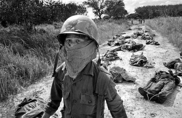 Южновьетнамский морпех в специальной повязке среди разлагающихся трупов американских и вьетнамских солдат, которые погибли в ходе боевых действий на каучуковой плантации в 70 км к северо-востоку от Сайгона, 27 ноября 1965 года.