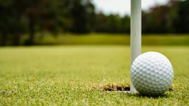 A golf ball sits just outside the cup on the green.