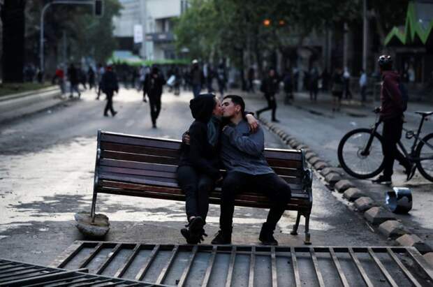 Пара на скамейке, оставленной демонстрантами во время протестов в Сантьяго.