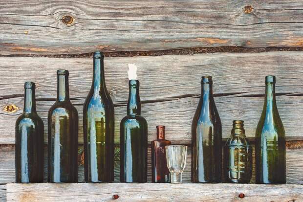 Old bottle of alcohol and a glass are on the background of wooden wall