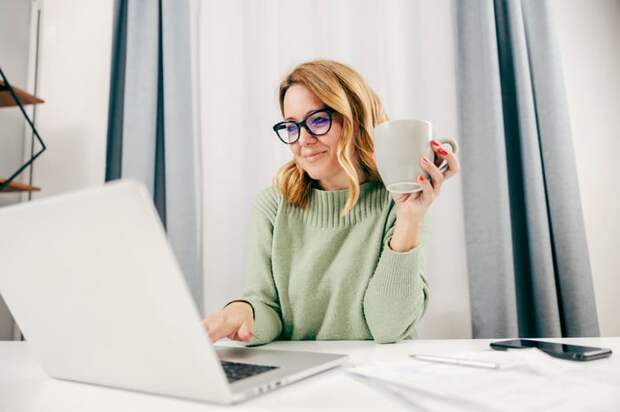 A person at a laptop is holding a mug.