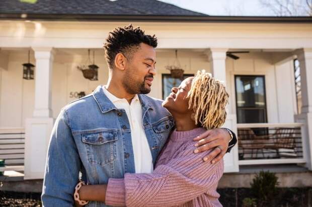 A couple embraces in front of their home.