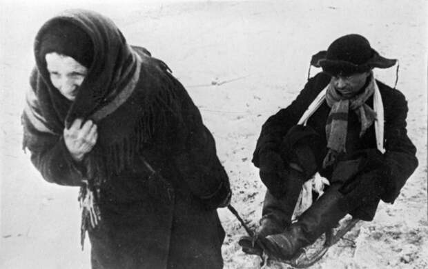 Жители блокадного Ленинграда: женщина везет ослабевшего от голода мужа на санках