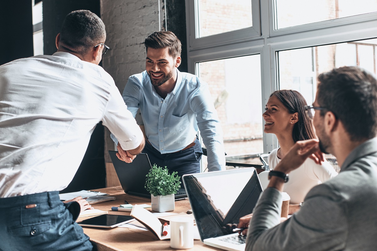 Young modern men in smart casual wear shaking hands and smiling while working in the creative office