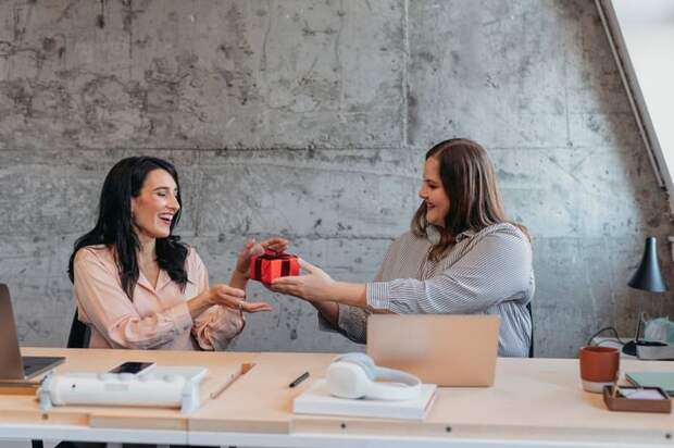 Female gives friend wrapped gift in an office setting.