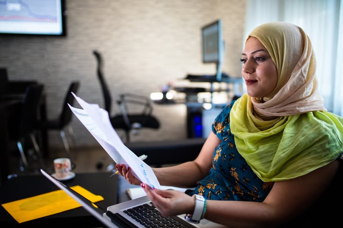 Person looking at documents while sitting in front of a laptop.