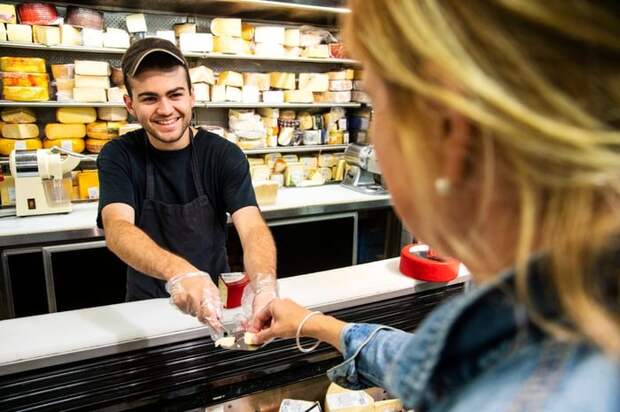 Employee handing sample of cheese to woman shopper.
