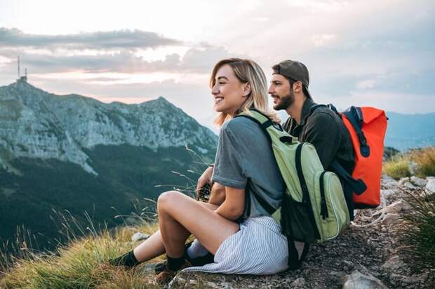 A man and woman resting and enjoying the view with backpacks on after completing a hike to a mountaintop.