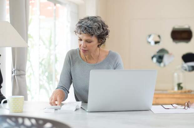 Adult sitting at table in front of computer is looking at receipts and paying bills.