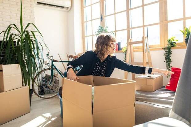 A young woman packing moving boxes in the living room of her sunny apartment.