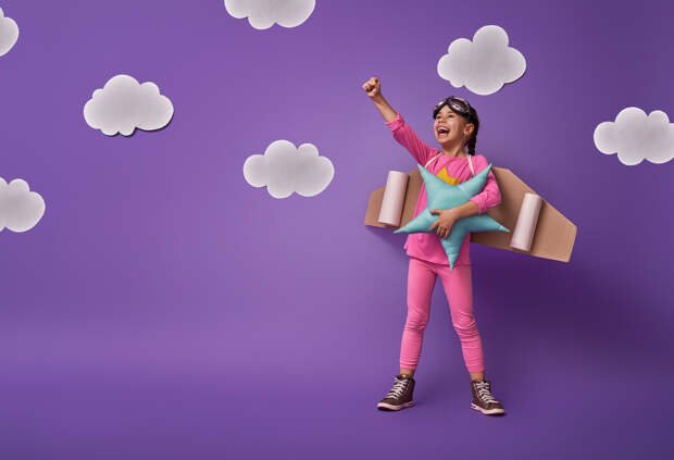 Little child girl in an astronaut costume is playing and dreaming of becoming a spaceman. Portrait of funny kid on a background of ultraviolet wall with white clouds.