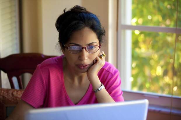 Serious person with hand on chin looking at laptop.