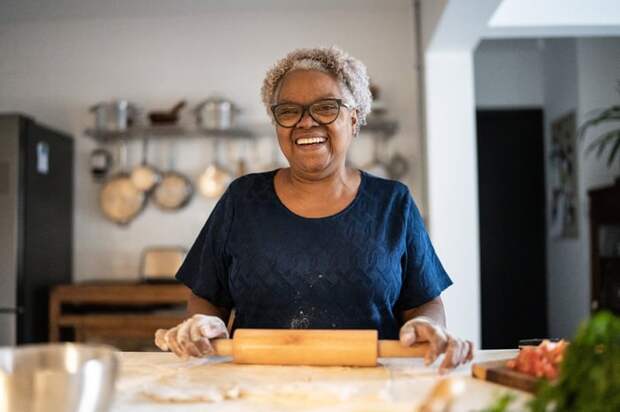 A smiling person rolling out pastry dough on a kitchen table.