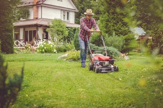 A man pushing a lawn mower with a house in the background.