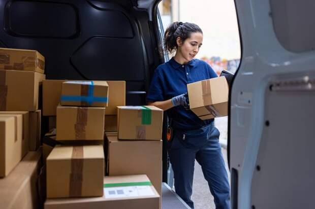 A woman checks a box in the back of a van full of boxes.