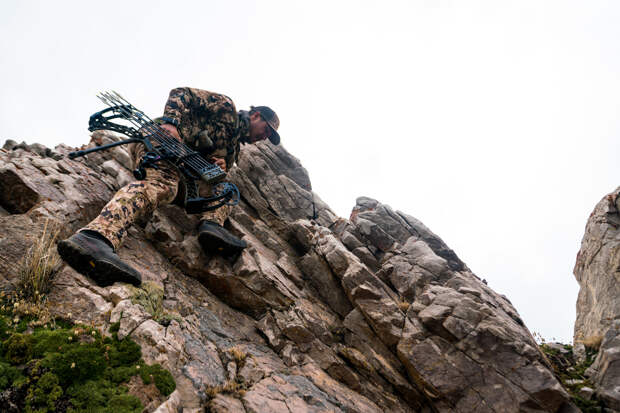 brett seng climbing across rocks with his hunting bow in camo
