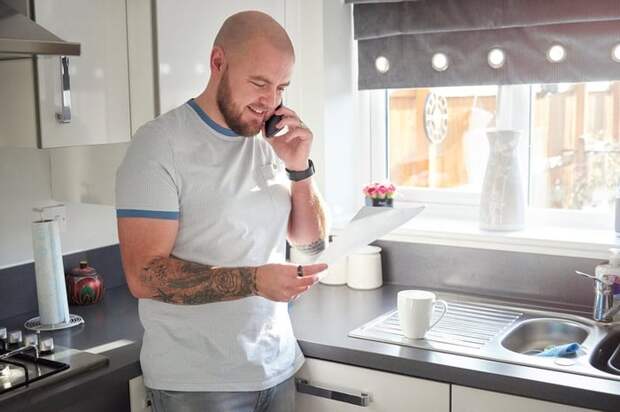 A homeowner stands in his kitchen and is on the phone with his loan servicer.