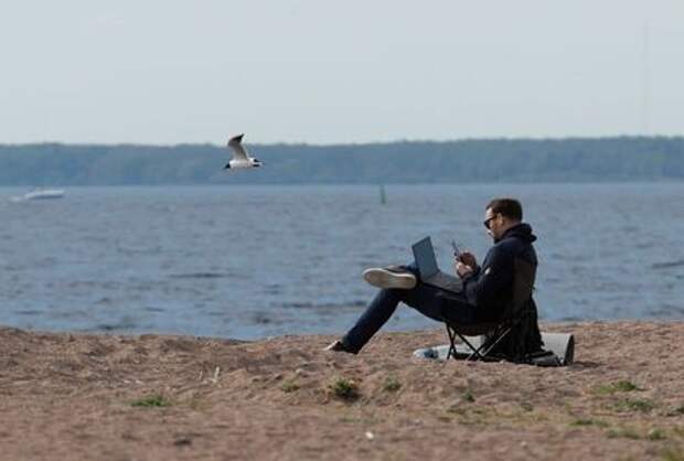 A man uses his smartphone and laptop as he sits on the shore of the Gulf of Finland amid the outbreak of the coronavirus disease (COVID-19) in Saint Petersburg, Russia May 27, 2020. REUTERS/Anton Vaganov