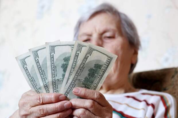 Older person holding a spread of five $100 bills.