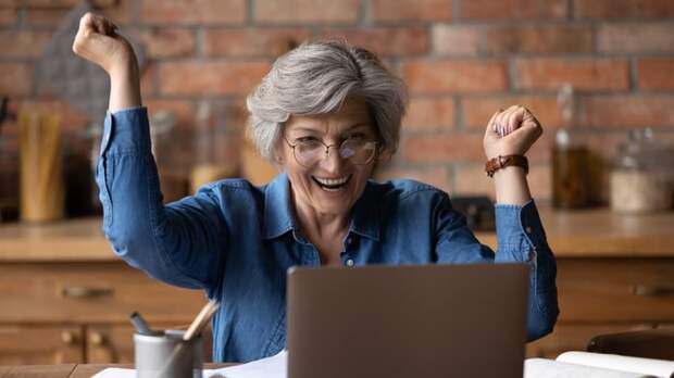 Older adult cheering while looking at their laptop screen.