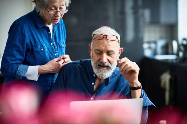 An older couple discusses something on a laptop screen.