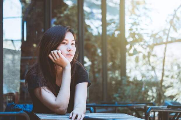 A young woman sitting outside with her chin resting in her hand.
