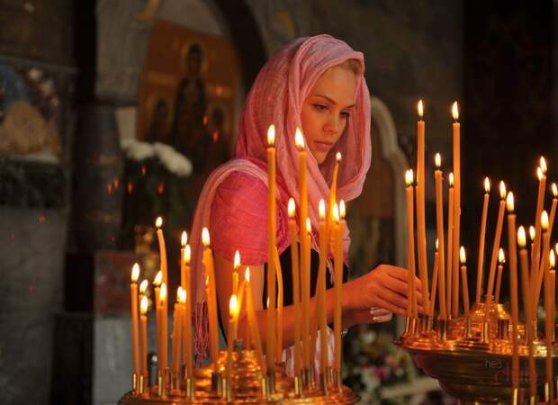 Девушка молится в церкви и ставит свечи