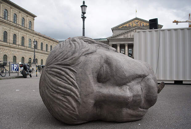 Сделанное из картона скульптурное изображение головы Ангелы Меркель перед зданием Баварской государственной оперы в Мюнхене — инсталляция к спектаклю «Блуждающие. Европейское разрушение»