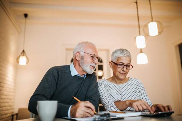 Retired couple reviewing their finances with paper and calculator while seated at a table.