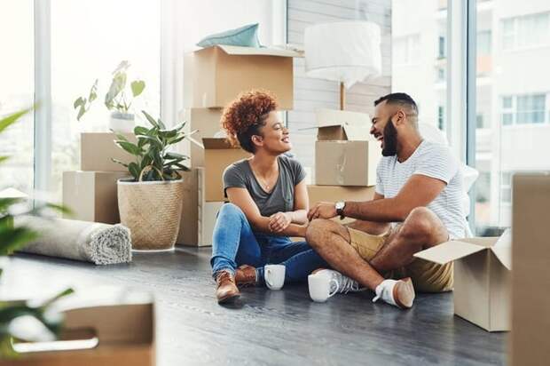 Two smiling people sitting on the floor between moving boxes.
