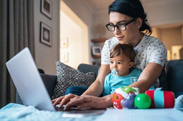 Parent sitting with toddler typing on laptop.