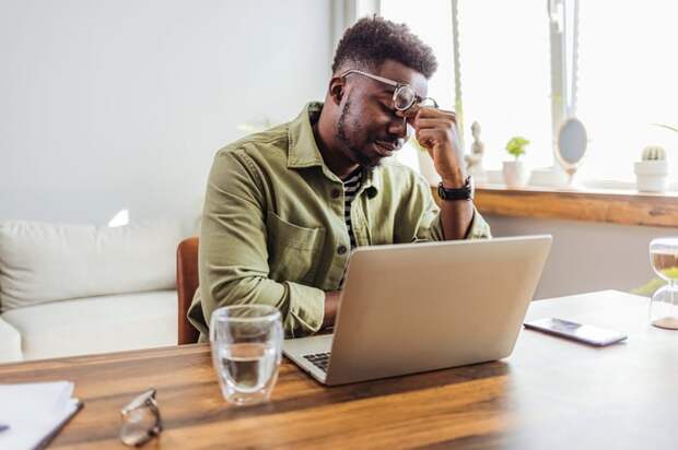 A person at a laptop pinching their nose.