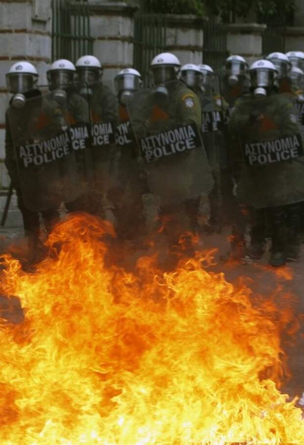 A group of riot policeman is stopped by flames caused by a petrol bomb thrown by protesters during clashes in central Athens