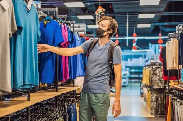 A man wearing a medical mask while shopping in a clothing store.