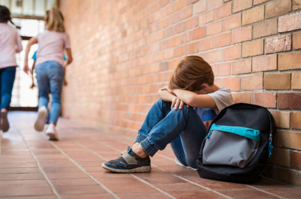 Как понять, что над ребенком издеваются в школе, и что делать, чтобы это предотвратитьLittle boy sitting alone on floor at school after being bullied