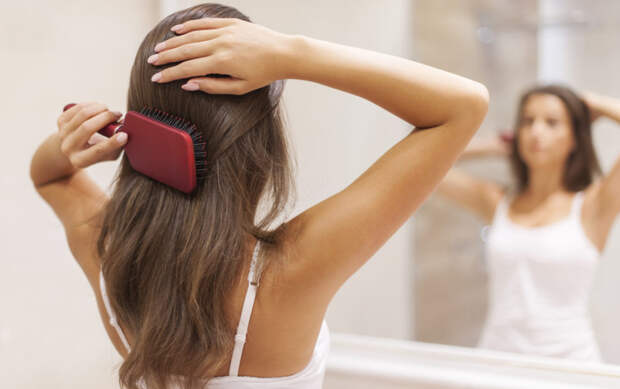 Young woman brushing healthy hair in front of a mirror