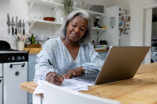Smiling person writing note while sitting in front of laptop.