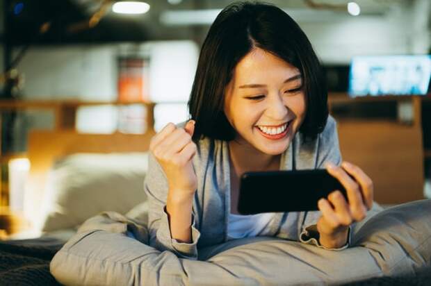 Smiling person lying on bed, looking at phone.