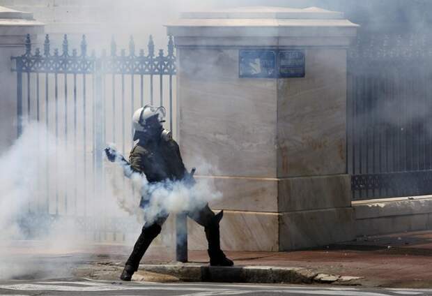 A policeman throws a teargas canister during clashes with protesters in Athens