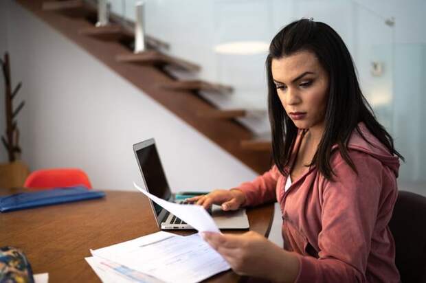 An adult sits at a desk at home looking through financial documents.