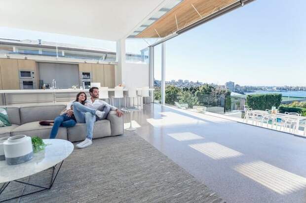 A smiling man and woman sitting on the couch in their large, open living room looking out at the expansive view.