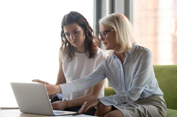 A financial advisor and her female client sitting together on a couch and looking at a laptop.