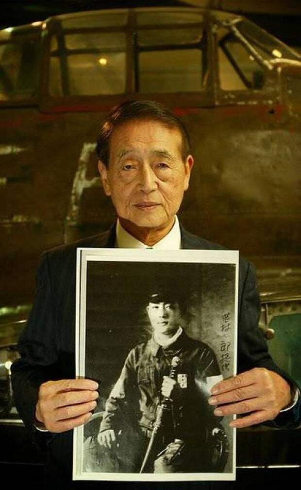 Бывший японский пилот-камикадзе Хичиро Наемура (Hichiro Naemura) держит в руках свой портрет военных лет, стоя возле истребителя “Mitsubishi A6M Zero”
