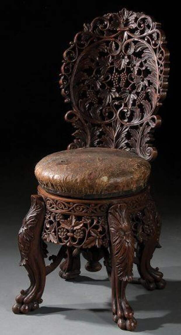 A VERY FINE CONTINENTAL CARVED WALNUT PIANO STOOL late 19th century, of adjustable height, with screw turned leather seat, allover pierced scrolling grape leaf and fruit carved cluster back above a seat raised on four claw footed legs.
