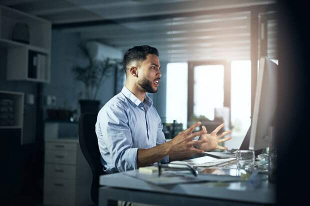 An angry person with hands outstretched looking at a computer monitor.