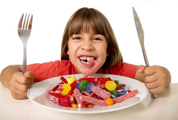 cute European female child smiling happy eating candy like crazy with fork and knife in sugar abuse , unhealthy sweet nutrition concept , children candy addiction and kids dental care