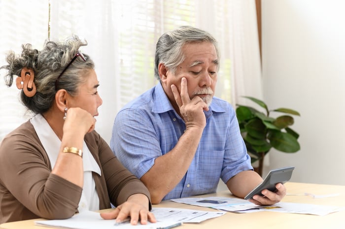 A visibly worried couple using a calculator to analyze bills and financial statements while seated at a table.