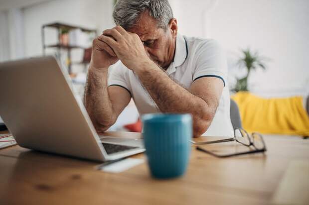 Stressed person with hand on head sitting in front of laptop.
