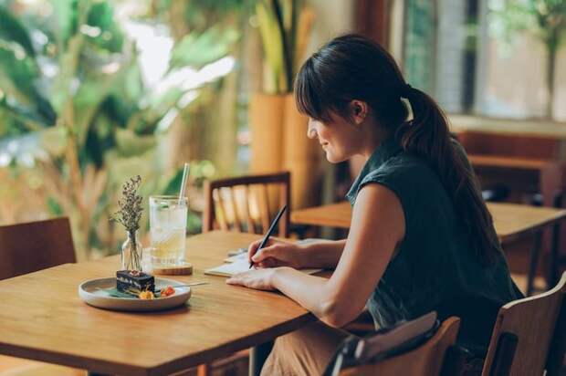 Woman writes letter at cafe table.