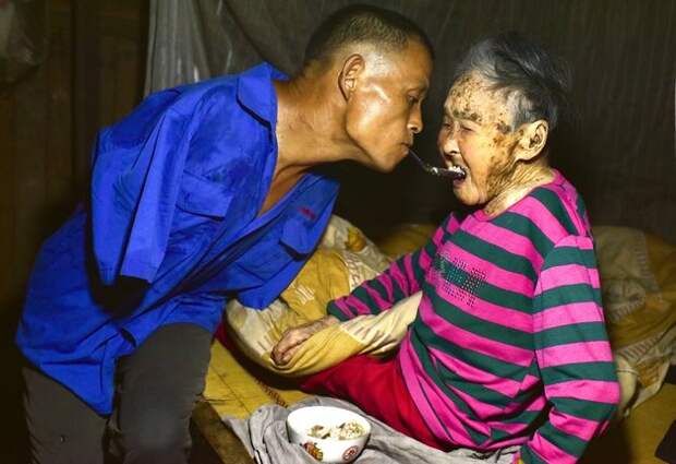 16 Aug 2015, Chongqing Municipality, China --- Chen Xingyin, a 48-year-old farmer who lost his arms at seven, left, holds a spoon in the mouth to feed his mother at his home in Tongxin village, Fengdu county, Chongqing, China, 16 August 2015. A 48-year-old farmer from Chongqing municipality who lost his arms in an accident when he was young has made headlines this week after his touching story of perseverance came to the attention of Chinese netizens. Chen Xingyin is from Tongxin village, Fengdu county, Chongqing municipality. He lost his arms in an electrical accident when he was only 7 years old. Despite this obstacle, Chen has managed to do his best to fend for himself. He can do most work on his own, including farming, cooking and feeding his goats.Chen is the youngest son from a six-member family. Since 2014, he has taken care of his bed-ridden 88-year-old mother, who began suffering from bronchitis five --- Image by © Imaginechina/Corbis